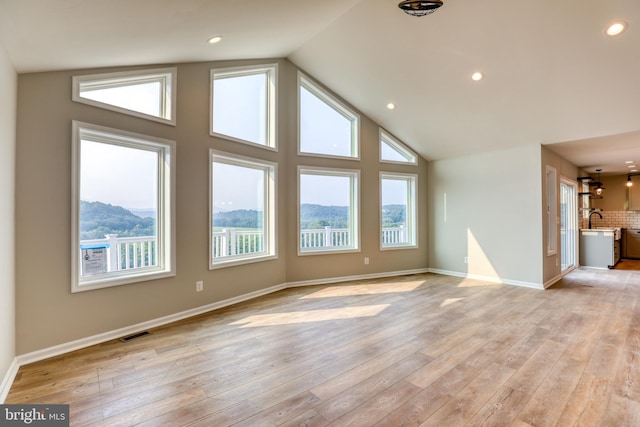 unfurnished living room featuring high vaulted ceiling, light hardwood / wood-style flooring, a mountain view, and sink