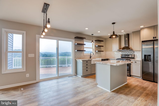 kitchen with wall chimney exhaust hood, a kitchen island, stainless steel appliances, and light hardwood / wood-style flooring