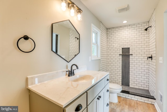 bathroom featuring vanity, a tile shower, wood-type flooring, and toilet