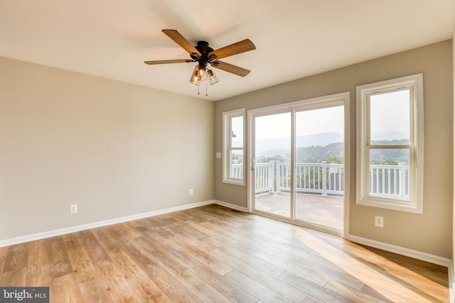 empty room with ceiling fan, light hardwood / wood-style flooring, and a mountain view