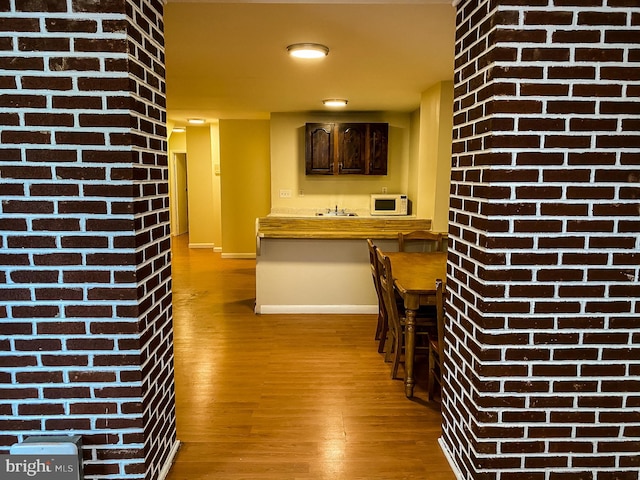 interior space with light hardwood / wood-style flooring, brick wall, and dark brown cabinetry