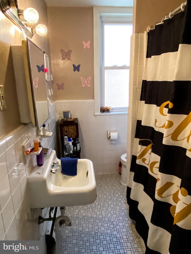 bathroom featuring toilet, tasteful backsplash, tile walls, tile flooring, and sink