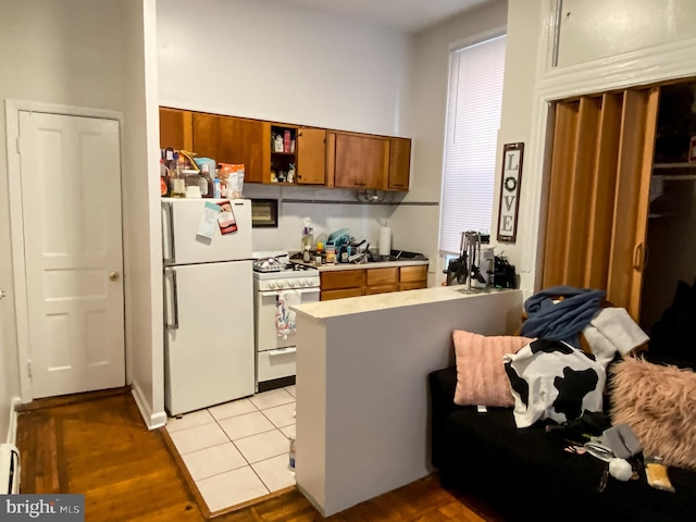 kitchen with kitchen peninsula, white appliances, light tile flooring, and baseboard heating