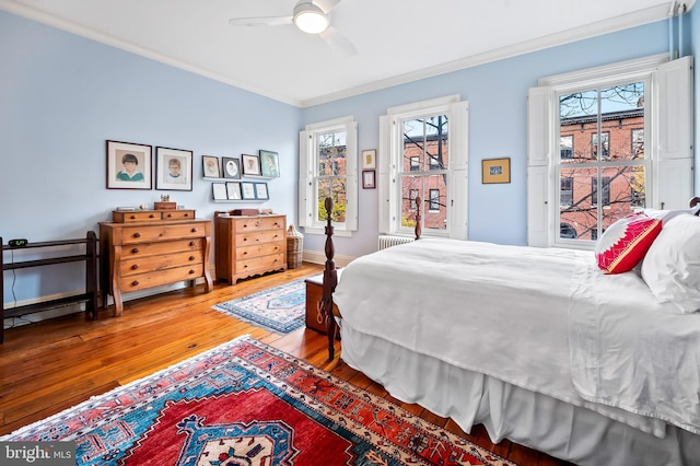 bedroom with crown molding, radiator heating unit, multiple windows, and hardwood / wood-style flooring