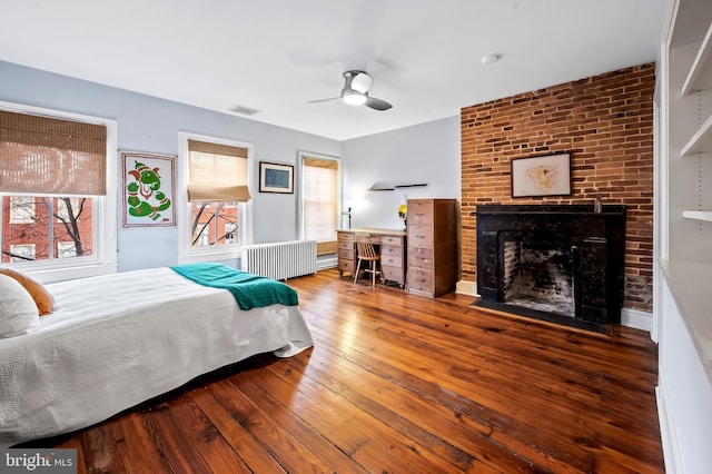 bedroom with ceiling fan, wood-type flooring, radiator, and a brick fireplace