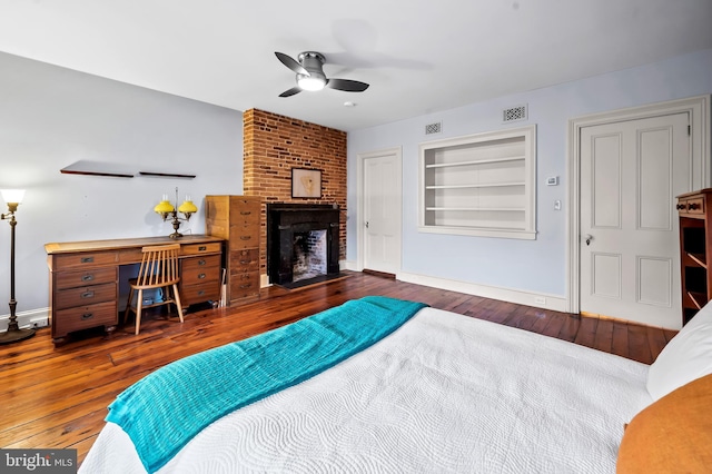 bedroom featuring a brick fireplace, dark hardwood / wood-style floors, and ceiling fan