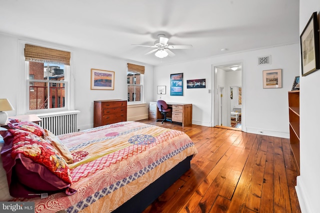 bedroom featuring wood-type flooring, radiator heating unit, ceiling fan, and built in desk