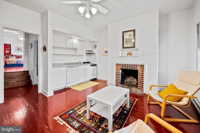 living room featuring ceiling fan, a brick fireplace, and dark hardwood / wood-style flooring