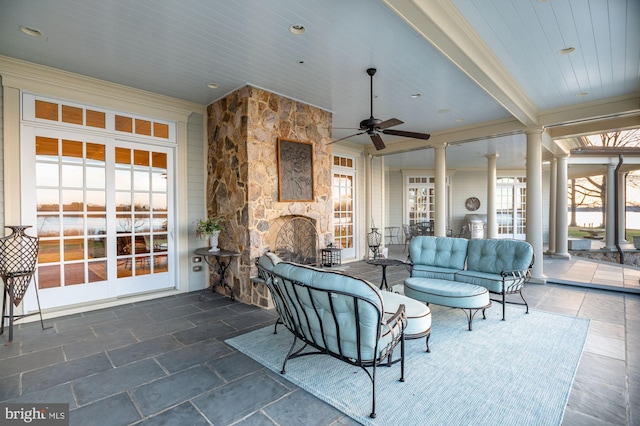 interior space featuring beamed ceiling, a stone fireplace, ceiling fan, and ornate columns