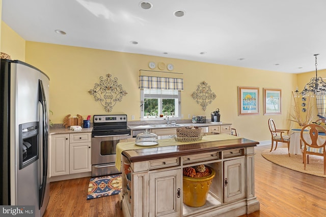 kitchen with light hardwood / wood-style floors, a kitchen island, appliances with stainless steel finishes, hanging light fixtures, and sink