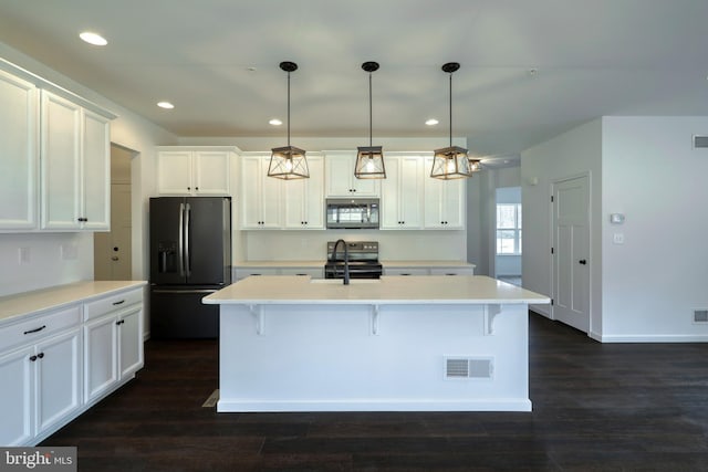 kitchen with stainless steel appliances, dark wood-type flooring, white cabinetry, hanging light fixtures, and a kitchen island with sink