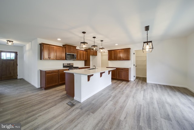 kitchen with a kitchen island with sink, hanging light fixtures, a breakfast bar area, light hardwood / wood-style floors, and stainless steel appliances