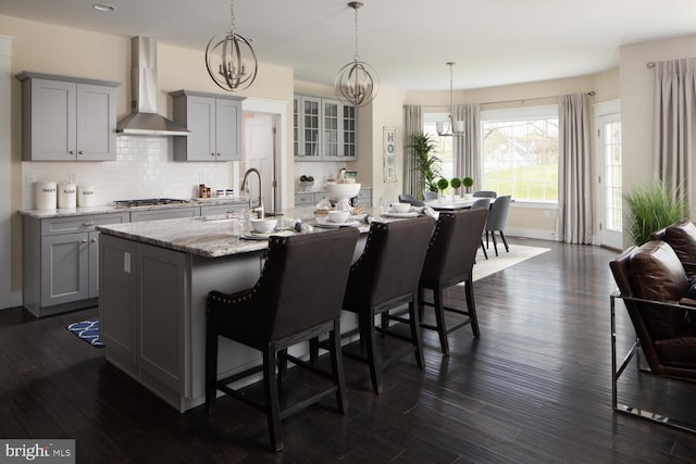 kitchen with wall chimney range hood, a kitchen bar, gray cabinets, dark hardwood / wood-style flooring, and a kitchen island with sink