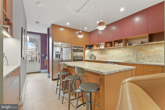 kitchen featuring pendant lighting, light hardwood / wood-style floors, a kitchen island, appliances with stainless steel finishes, and sink