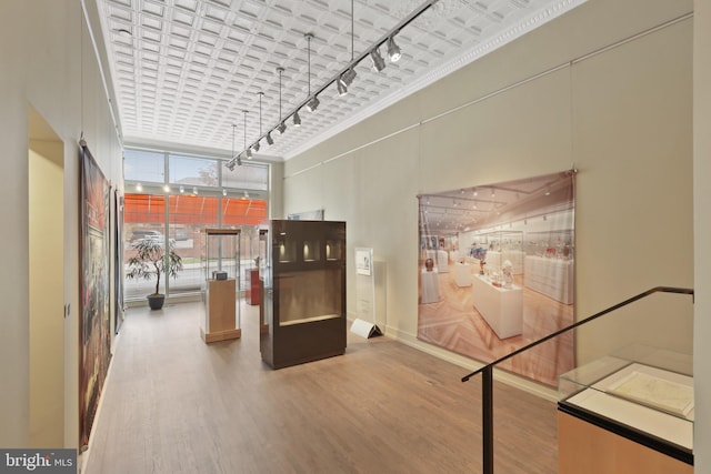 corridor with light wood-type flooring, a high ceiling, and rail lighting