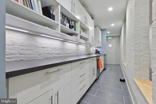 kitchen featuring dark tile floors, dishwasher, sink, and white cabinetry