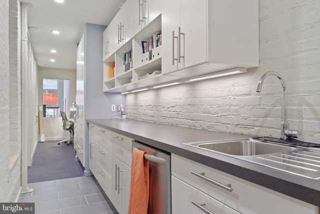 kitchen featuring stainless steel dishwasher, sink, dark tile floors, and white cabinetry