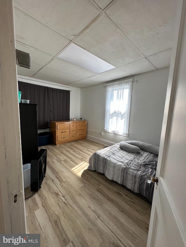 bedroom with a drop ceiling and light wood-type flooring