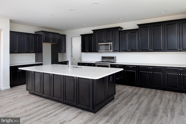 kitchen with stainless steel appliances, sink, a center island with sink, and light hardwood / wood-style flooring