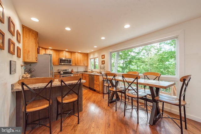 kitchen with appliances with stainless steel finishes, a kitchen breakfast bar, kitchen peninsula, light hardwood / wood-style flooring, and light stone countertops