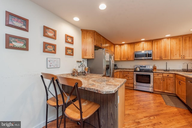 kitchen with stainless steel appliances, kitchen peninsula, light hardwood / wood-style flooring, a breakfast bar area, and light stone counters