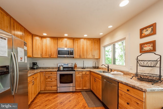 kitchen featuring appliances with stainless steel finishes, light hardwood / wood-style floors, light stone countertops, and sink