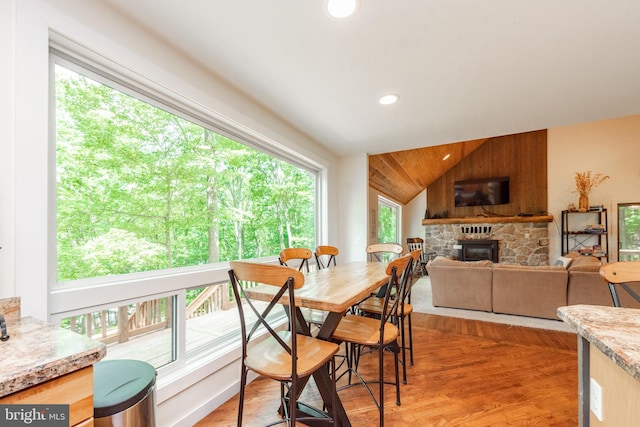 dining space with wooden walls, lofted ceiling, light hardwood / wood-style floors, and a fireplace