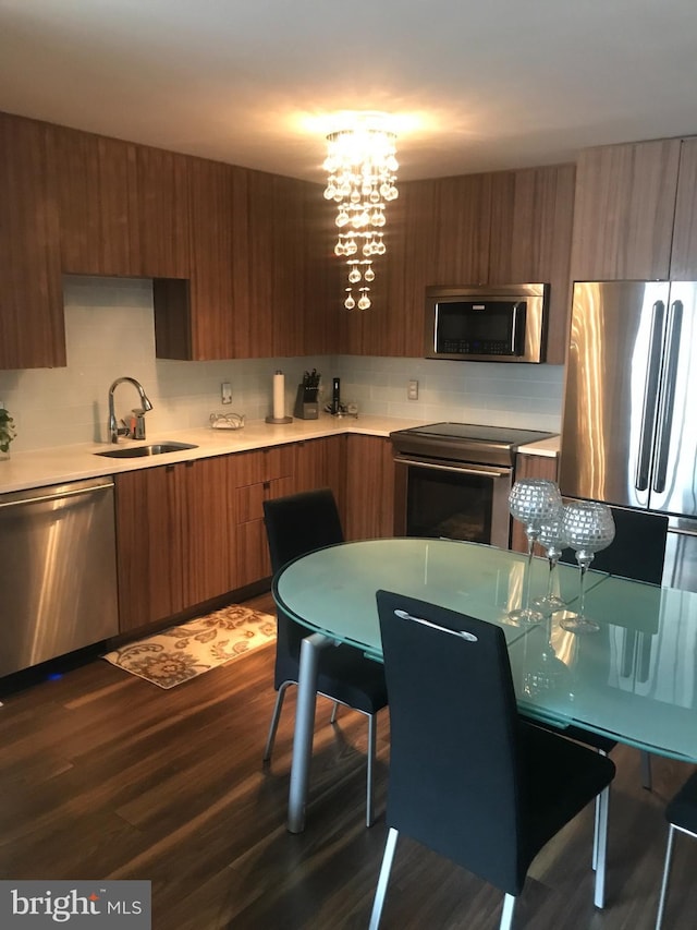 kitchen featuring stainless steel appliances, an inviting chandelier, tasteful backsplash, dark wood-type flooring, and sink