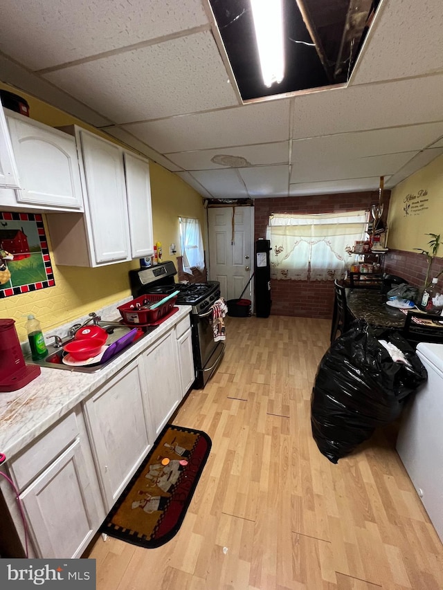 kitchen with white cabinets, stainless steel range with gas cooktop, light hardwood / wood-style floors, and a drop ceiling