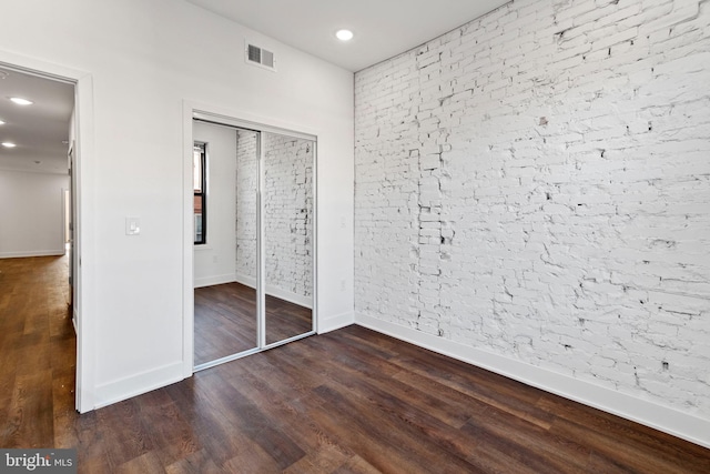 unfurnished bedroom with brick wall and dark wood-type flooring