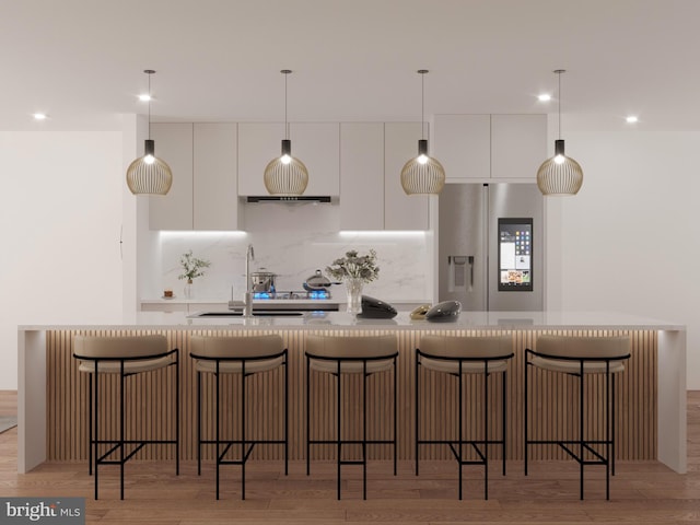 kitchen with white cabinets, light hardwood / wood-style floors, stainless steel fridge with ice dispenser, and a kitchen bar