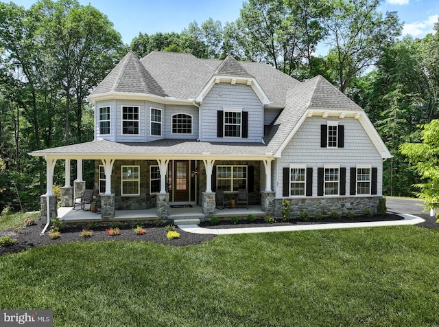 view of front of home with stone siding, a shingled roof, a porch, and a front yard