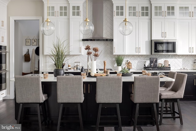 kitchen with wall chimney range hood, decorative backsplash, white cabinetry, and appliances with stainless steel finishes