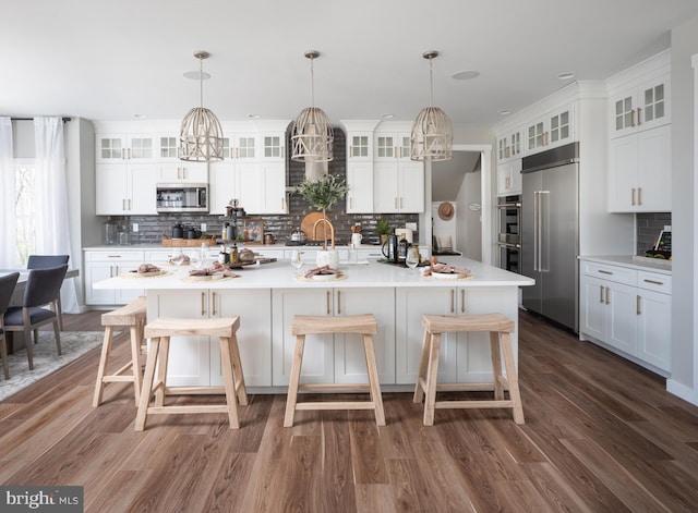 kitchen with stainless steel appliances, decorative light fixtures, decorative backsplash, a center island with sink, and dark hardwood / wood-style flooring