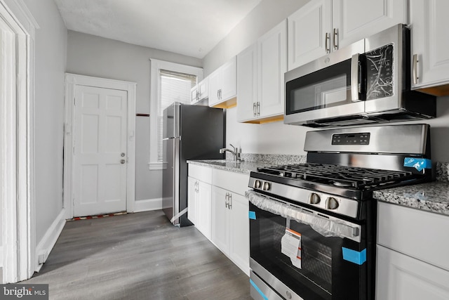 kitchen featuring appliances with stainless steel finishes, light stone countertops, white cabinetry, and dark hardwood / wood-style floors