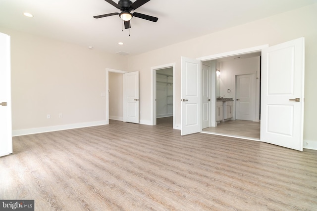 unfurnished bedroom featuring a closet, ceiling fan, ensuite bath, light wood-type flooring, and a walk in closet