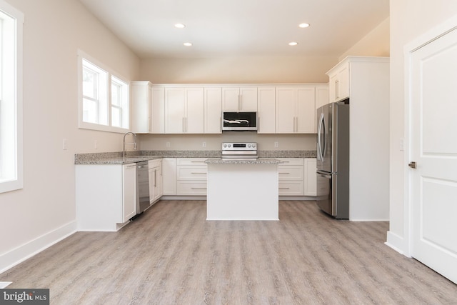 kitchen featuring white cabinets, stainless steel appliances, light hardwood / wood-style floors, and light stone counters