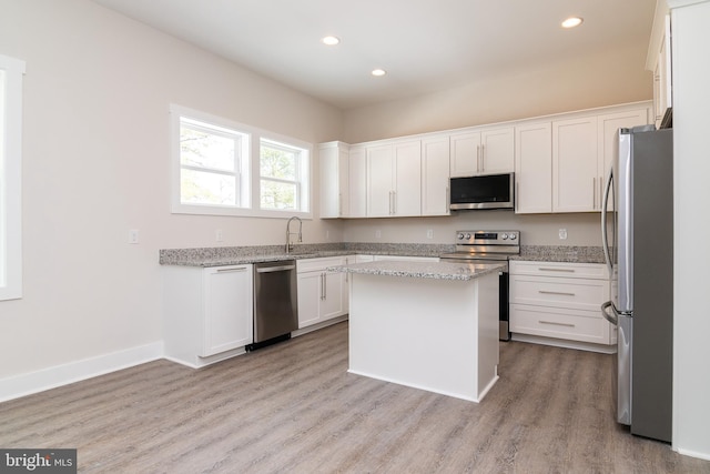 kitchen with white cabinetry, light stone counters, a kitchen island, appliances with stainless steel finishes, and light hardwood / wood-style flooring