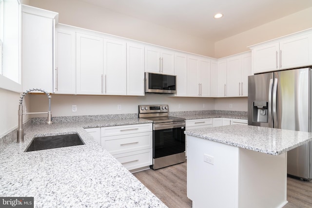 kitchen with white cabinetry, light hardwood / wood-style flooring, a kitchen island, appliances with stainless steel finishes, and sink