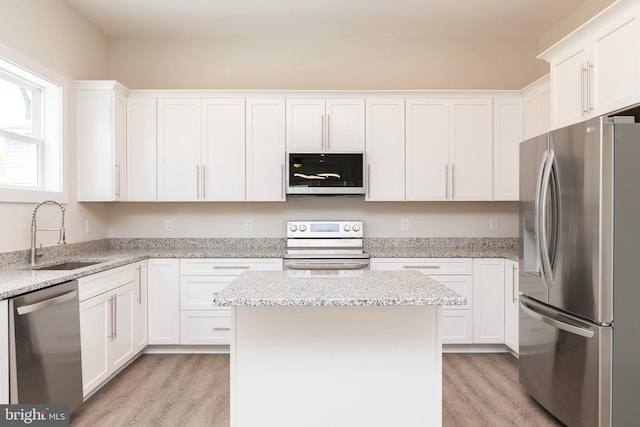 kitchen with a center island, light hardwood / wood-style floors, light stone countertops, appliances with stainless steel finishes, and sink