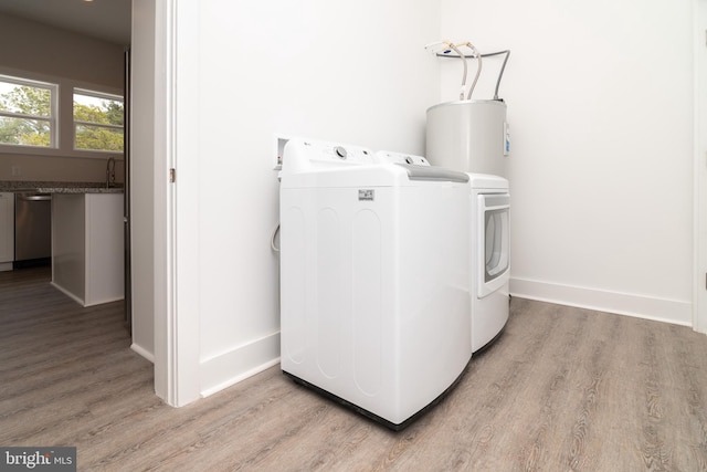 laundry room with electric water heater, sink, light hardwood / wood-style flooring, and washing machine and clothes dryer