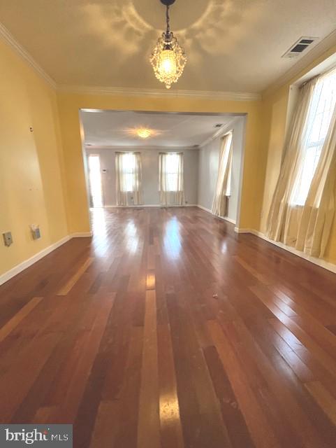 empty room featuring dark hardwood / wood-style flooring, ornamental molding, and a chandelier