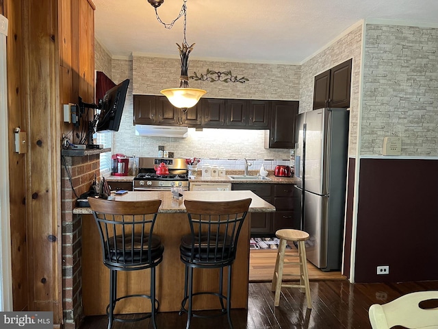 kitchen featuring a breakfast bar area, stainless steel appliances, decorative light fixtures, sink, and dark hardwood / wood-style floors