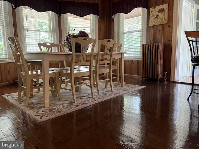 dining room featuring radiator heating unit, wood walls, and dark wood-type flooring