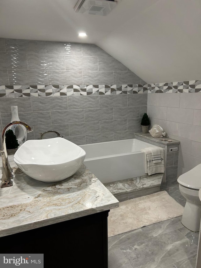 bathroom featuring toilet, tile flooring, vanity, tile walls, and vaulted ceiling