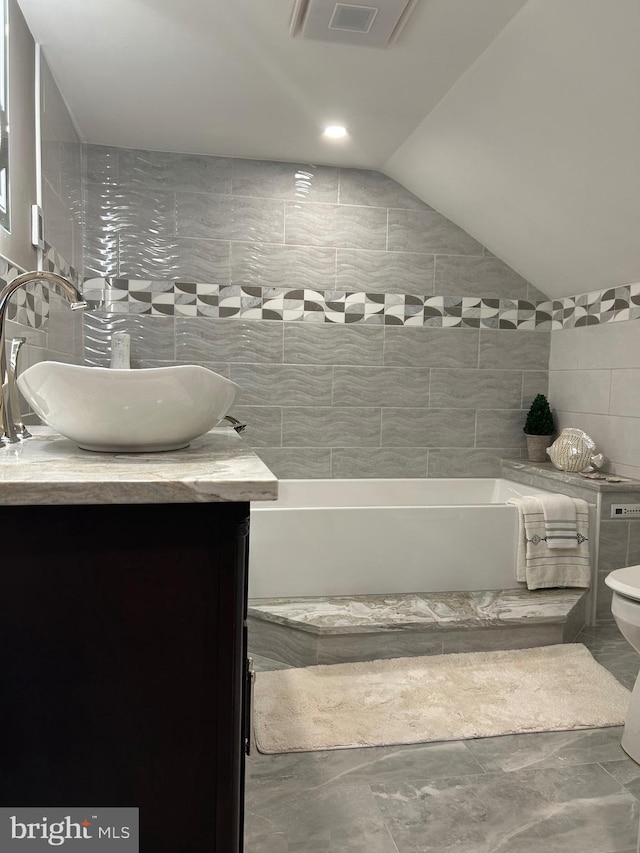 bathroom with toilet, tile flooring, vanity, lofted ceiling, and tile walls