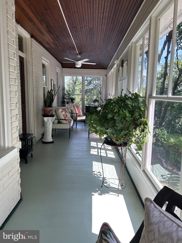 unfurnished sunroom with a wood stove, ceiling fan, and wooden ceiling