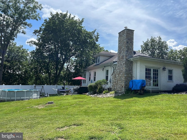 rear view of property featuring a lawn, a fenced in pool, and french doors