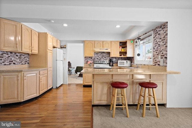 kitchen featuring a kitchen bar, tasteful backsplash, light brown cabinetry, light hardwood / wood-style flooring, and white appliances