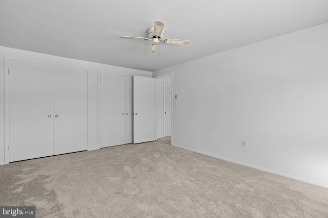 unfurnished bedroom with two closets, ceiling fan, and light colored carpet